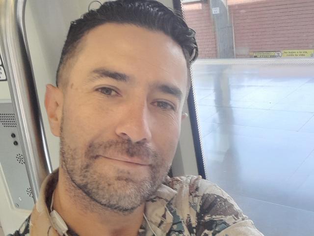 Arsoleros has short, dark hair, a light beard, and is wearing a camouflage shirt. He's sitting on a bus, looking at the camera with a slight smile.
