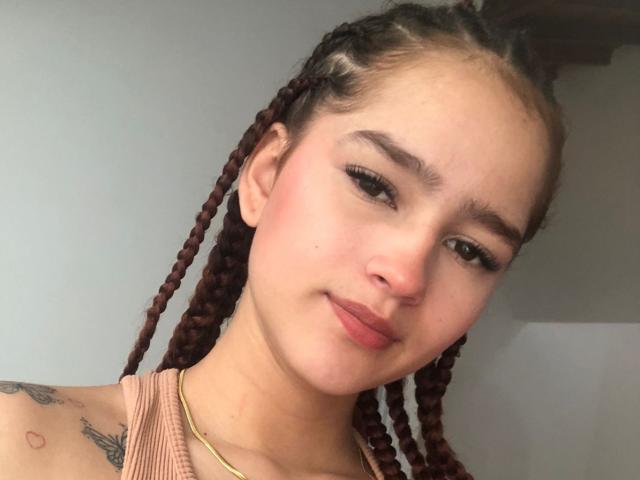 Melody Mansson heeft bruin gevlochten haar, een lichte huid en een kleine neus. Ze draagt een roze top, een gouden ketting en heeft tatoeages op haar schouder. Haar borsten zijn klein..