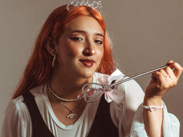 IsabellaClown with red hair, wearing a sparkly tiara, holding a jeweled wand, smiling, white shirt, black dress, necklace, earrings, and ring, soft lighting, gentle expression.