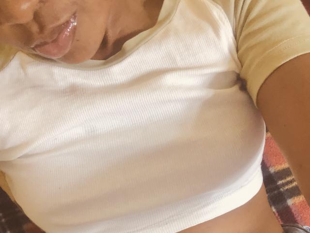 Lillah's white ribbed shirt is tight, showing her small tits and glistening wet lips. Her tan skin is visible, and the image is a selfie from above.