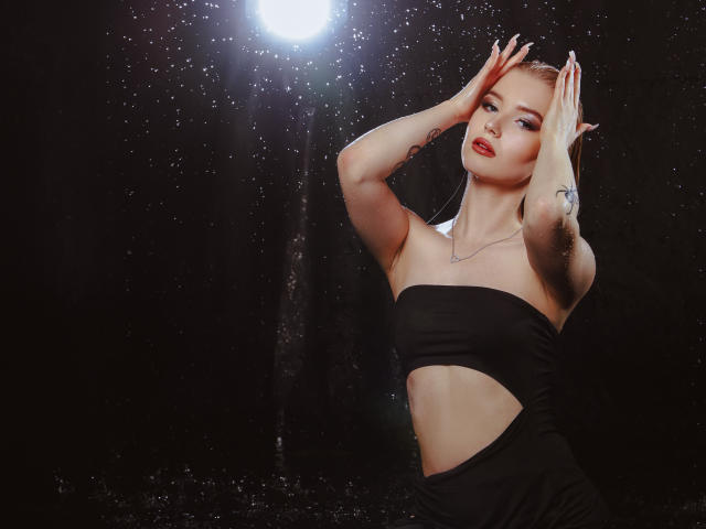 NicoleBrian with pointy elf ears, hands on head, black strapless cutout dress, glowing light, red lipstick, tattoo on right arm, wet skin, sexy, dark background.