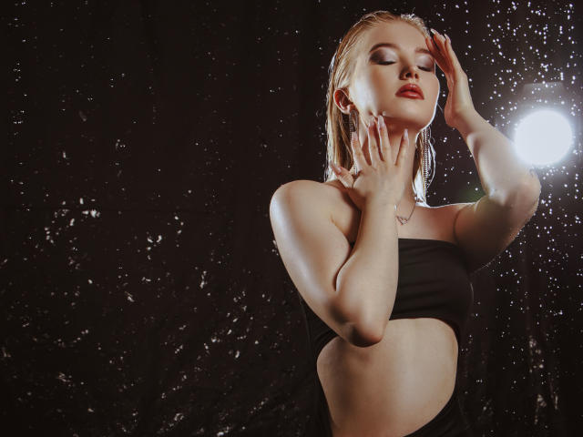 NicoleBrian with wet blonde hair, eyes closed, black tube top, hands on neck, water splashing, bright light source, sexy, attractive, slim, pale skin, red lipstick, nipples visible.