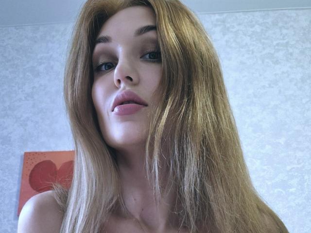 Angelovna has long, straight brown hair, light skin, and pink lips. She's looking at the camera with a slight smile. Her tits are not visible.