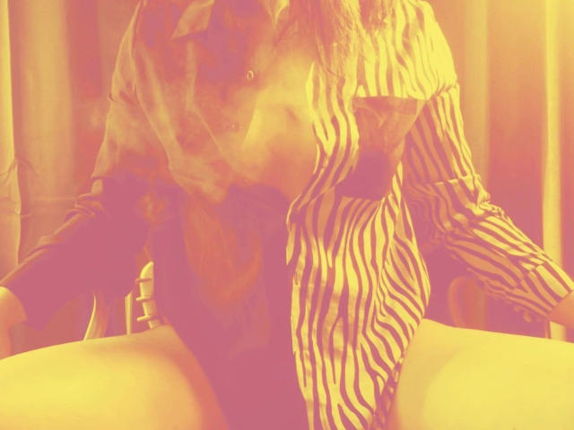 ScorpionLady-hot is wearing a striped shirt, kneeling with her ass up, being kissed by another person with their face close to her pussy. Warm yellow filter.