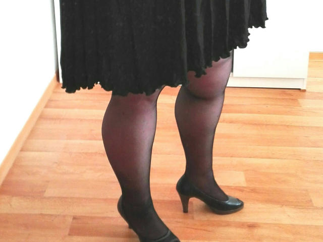 Meike4you-hot's legs in black sheer pantyhose and black high heels, standing on wooden floor, wearing a black skirt that's slightly ruffled at the bottom.