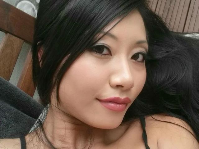 Lady-Tyra has black hair, Asian features, and a cute smile with pink lipstick. She's wearing a black top, and her face is centered in the photo.