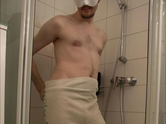 A shirtless Sweetbody23-hot with a towel wrapped around their ass, standing in a shower, wearing a white blindfold, and having a slightly hairy chest.