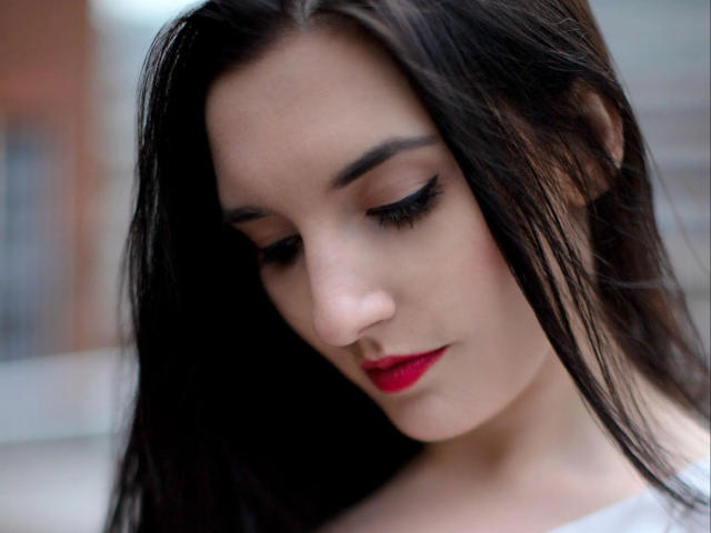 AlinaLamour-hot has dark straight hair, red lipstick, and black eyeliner, looking down with a soft, pretty face and subtle makeup, showing her smooth, fair skin and sexy look.