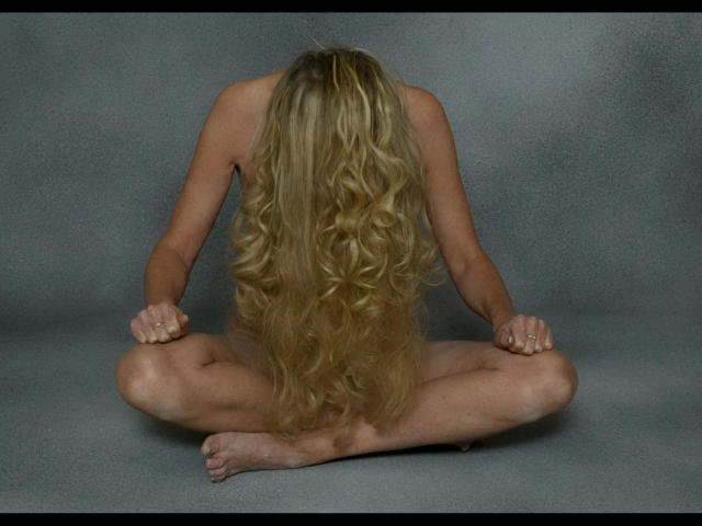 Pussycat0-hot is sitting nude with long, wavy blonde hair covering her back, arms folded over her knees, and legs crossed. She's on a gray floor.