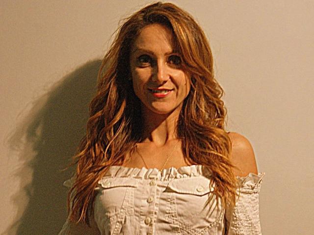 LarisaRais-hot with wavy, brown hair, smiling, wearing a white off-shoulder top, showcasing her small tits and buttoned chest. Her skin is tan, and she's looking cute.