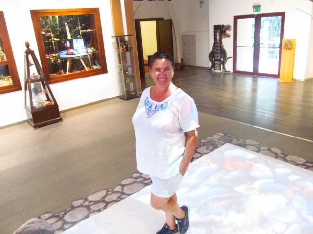 EmmaHotSquirt-sex, middle-aged woman with small tits, white shirt, blue embroidery, gray shorts, black shoes, smiling, standing, dark hair, indoor, wooden floor, glass door, wooden frame.