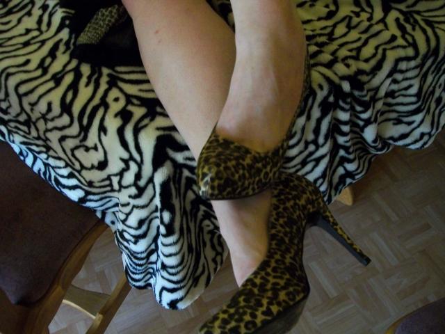 Hotferkel-sex's legs crossed, wearing leopard print high heels, on a zebra-striped blanket, showing pale skin and wooden floor.