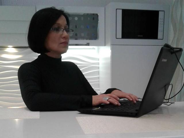 Sophia01-hot with black bob, glasses, and black turtleneck, typing on a black laptop with both hands, showing her tits slightly through her sleeves, in a white kitchen.