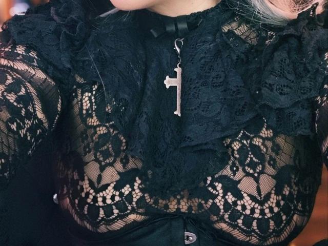 ScorpionLady-hot wears a black lace top, her tits visible through the patterned fabric, with a silver cross necklace hanging in the center. Her blonde hair is partially visible.