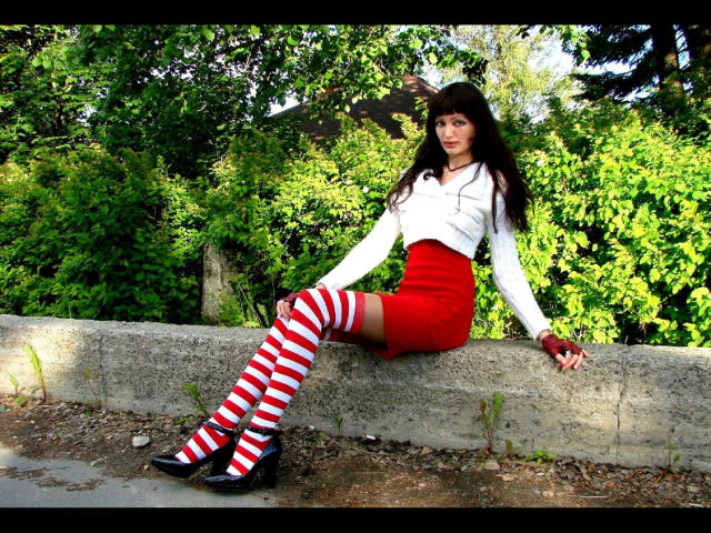 SexyNat-hot with striped red and white thigh-high socks, white top, red skirt, black heels, and long dark hair, sitting on a concrete wall, showing her ass.
