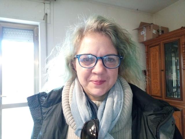 CuteDebby-hot with blue glasses, curly light-green hair, black jacket, gray scarf, and black sunglasses, smiling softly. Her tits are small, and she has a cute face.