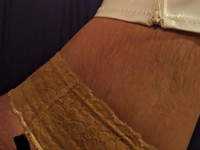Bootsica-hot's thigh with visible hair, wearing a lace-topped, brown, sheer panty, and a white garter, shown in a detailed, close-up shot.