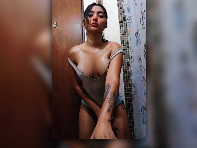 PauletteRoy with medium tits, black lace lingerie, tattoos on arms, smiling, brown hair, standing in marble-tiled shower, hand in hair, reflection in mirror.