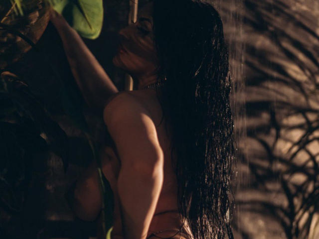 ClaireWarner with wet black hair, nude, back to camera, holding leaf, rain, dark, moody, small bare ass, necklace, shadowy, sensual, soft light, skin glistening.