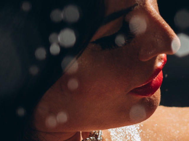 ClaireWarner's face with red lips, dark eyelashes, and shiny skin, showing a side profile with bokeh light spots, looking serious and sexy.