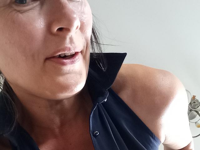 ClementineFoxy's face, showing a slight smile with visible wrinkles and a small metal piercing on her lower lip. She's wearing a dark blue, button-up shirt with a high collar.