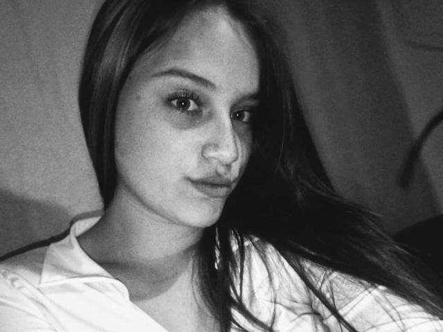 Black-and-white photo of TaniaCooper69 with long dark hair, small nose, and subtle smile, wearing a white shirt, looking slightly to the side, with a relaxed, confident expression.