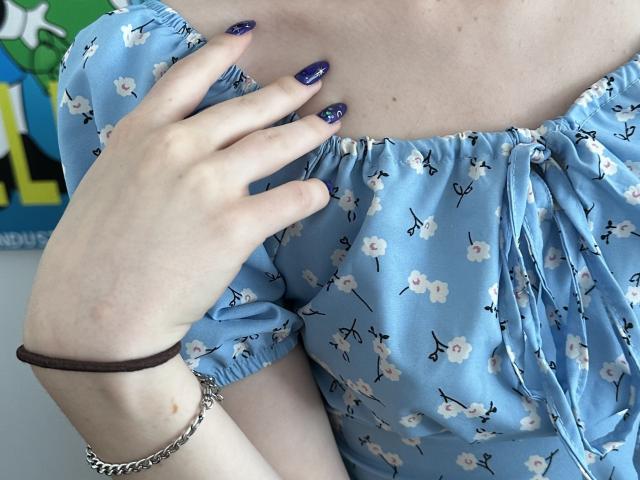 Valissia's light blue floral dress, showing her tits, with purple nail polish, brown wristband, and silver chain, touching her chest. Her skin is pale, and she's partially visible.
