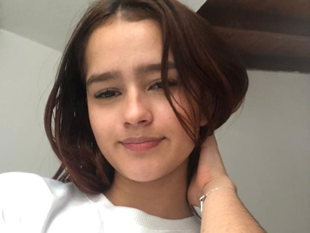 MelodyMansson has brown hair, light skin, and a cute smile. She's wearing a white shirt, and her hand's on her head, showing a silver bracelet.