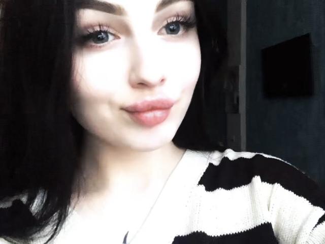 RickyLaze has pale skin, black hair, blue eyes, and pink lips. She's wearing a black and white striped top, looking at the camera with a slight smile.