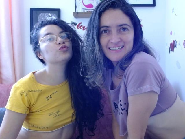 LunaVenus with glasses, yellow crop top, and long black hair pouts. LunaVenus with brown hair, pink shirt, and exposed tits smiles. Both have cute faces, white skin.