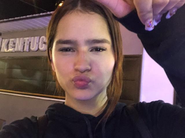 MelodyMansson with pouty lips, brown hair, black hoodie, and a hand touching her head, showing off her small nose and slightly parted pink lips in a selfie.