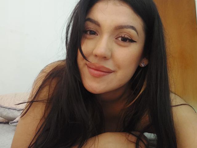 LauraRichis has long black hair, dark eyeliner, and a slight smile. She's lying on a bed, showing her bare shoulders and a cute nose ring. Her tits are not visible.