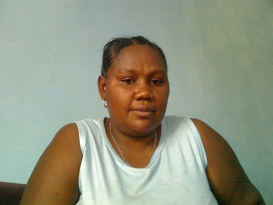 FafaOne is a chubby Black woman with braided hair, wearing a white tank top and small earrings, sitting and looking slightly to the side with a neutral expression.
