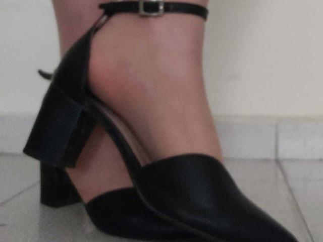 JackyEmma's ass is in a black, pointed-toe, high-heeled shoe with a thick, chunky heel and a small buckle strap on the ankle. Her foot is on a tile floor.