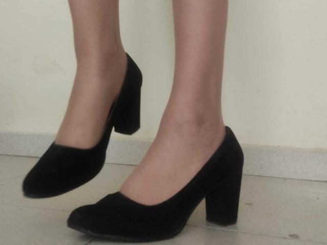 JackyEmma's legs wearing black, low-heeled, suede shoes with a slightly pointed toe, standing on a gray, textured floor. Her skin is light and smooth.