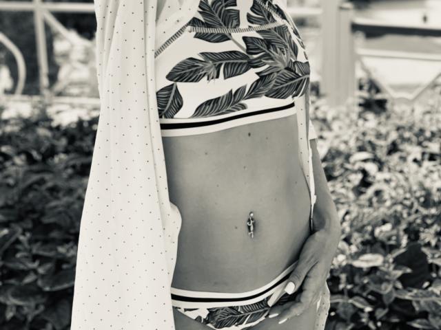 BelleLisaG's bare midriff showing leaf-patterned bra and panties, a polka-dotted shirt draped over, and a belly button piercing. Her hand rests on her lower belly.