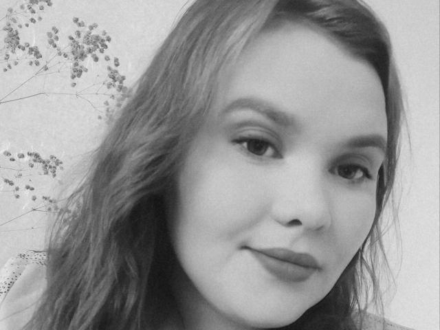 Black-and-white photo of MilaiDex with wavy hair, light skin, subtle smile, and slightly parted lips. MilaiDex's eyes are half-open and she's looking at the camera.