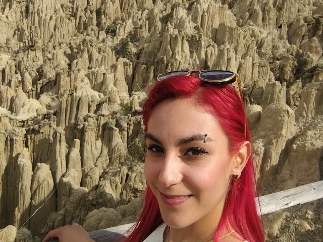 AmyStreetwise69 has bright red hair, black eyeliner, and eyeshadow, with small facial piercings, wearing sunglasses on her head, smiling at the camera.