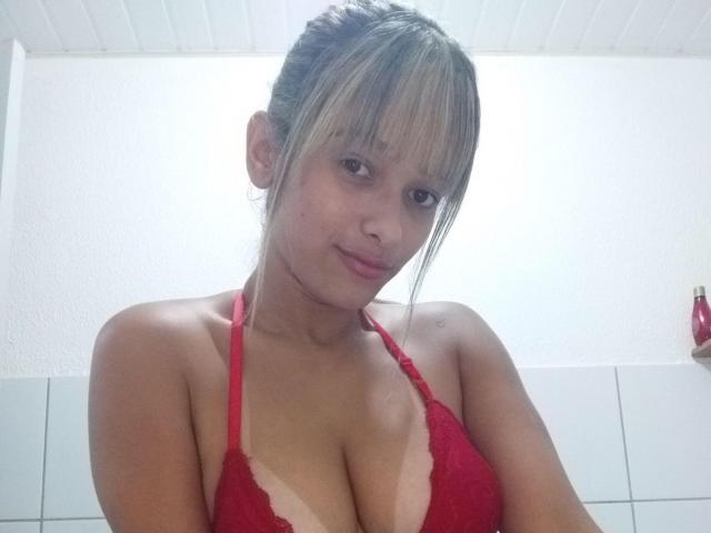 MarryCassol with light brown hair in a bun, wearing a red lace bra that reveals her large, tan-lined boobs, smiling softly at the camera.