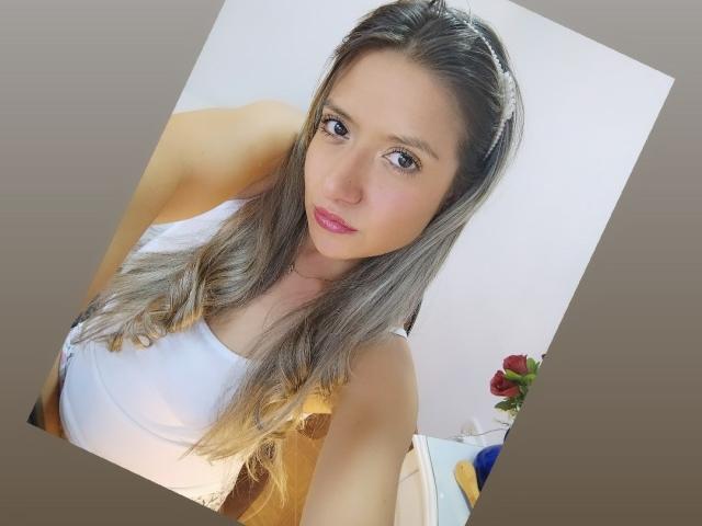ValeriaHunter69 with long, wavy blonde hair, pink lipstick, and white tank top, showing her tits in a selfie, looking at the camera with a slight smile.