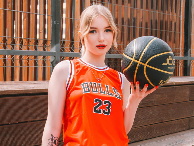 NicoleBrian, blonde, with red lipstick, holding a basketball, wearing an orange Bulls jersey with 23, has a tattoo on her right arm, and a necklace, standing outdoors.