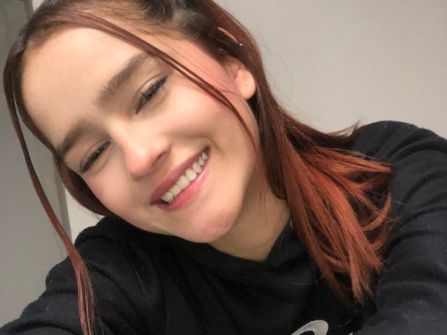 MelodyMansson's smiling face, slightly wavy brown hair, and small nose are visible. She's wearing a black hoodie, and her eyes are half-closed, showing a relaxed expression.