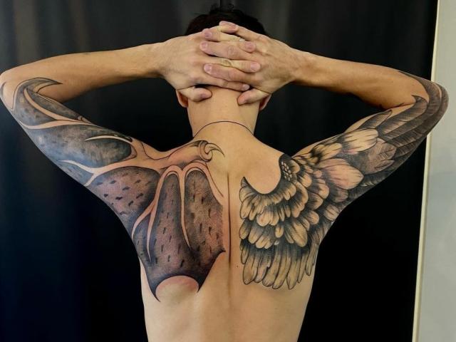 StormBernard's back is a tattooed work of art with a large, detailed wing on the right and a dark, textured, fish-like design on the left. Hands are behind head.