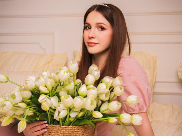 JuliaKing with long brown hair, pink dress, holding white tulips, looking at camera, subtle smile, pink nail polish, wavy hairband, soft lighting, pretty, feminine, gentle.