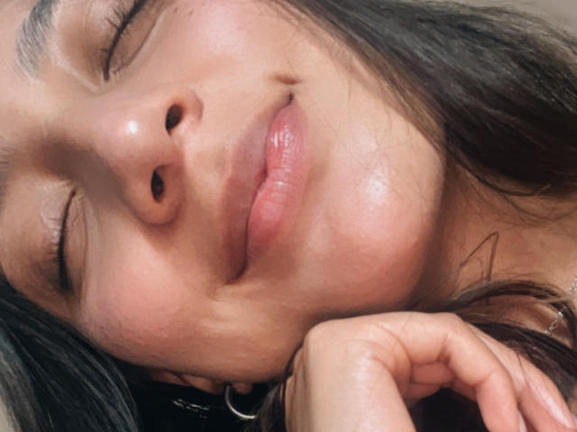 DianaFernandezz's face, slightly tilted, with closed eyes and a gentle smile. She's resting her chin on her hand, showing shiny, pinkish lips and a small nose.