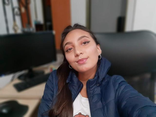 DianaFernandezz, con le labbra tumefatte, gli occhi marroni e i lunghi capelli castani, indossa una giacca imbottita blu scuro, piccoli orecchini a cerchio e una camicia bianca, in un selfie..
