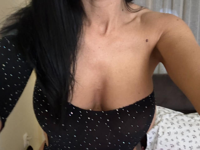 AndraD's black, sparkly, mesh top with a deep cut, showing her big, round tits. She's got long black hair, and a tattoo on her left arm.