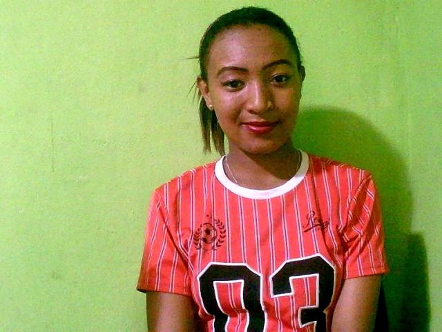 Mickayah with dark skin, small nose, and brown eyes, wearing a red and white striped football jersey with number 93, smiling slightly, standing against a green wall.