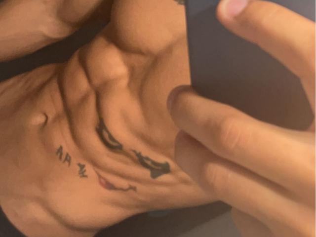StevenCum's muscular, tan-skinned torso with a black tattoo of a lion and Latin letters on his ribcage. A hand points to the tattoo.