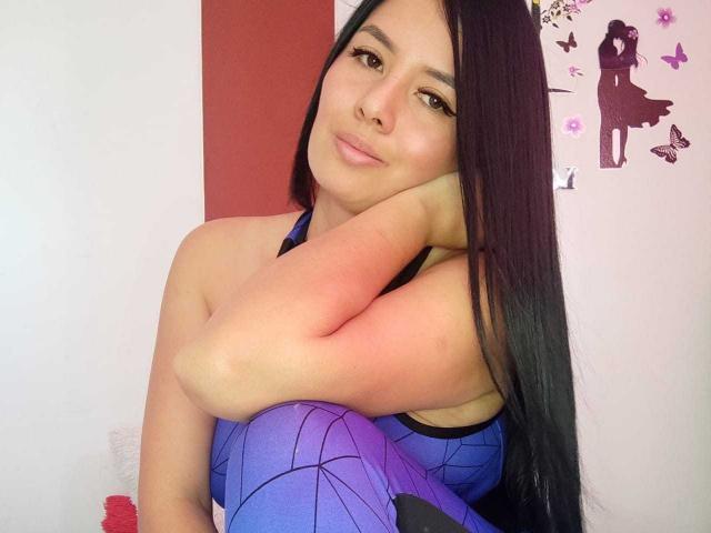 VenuzLove with long black hair, wearing a blue and purple spiderweb-patterned dress, smiling, resting her chin on her arm, showing her small tits, in a cute selfie.